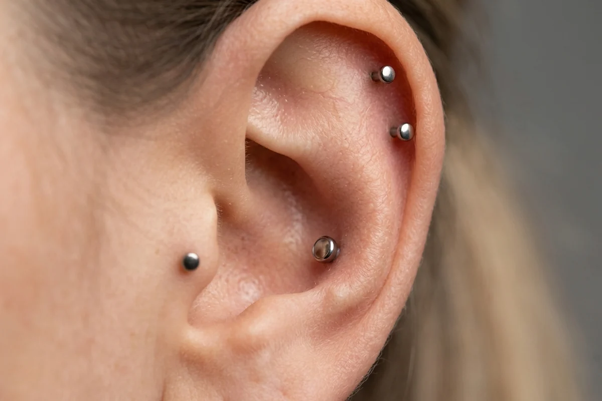 Human ear showing helix, tragus, and conch cartilage piercings with titanium studs