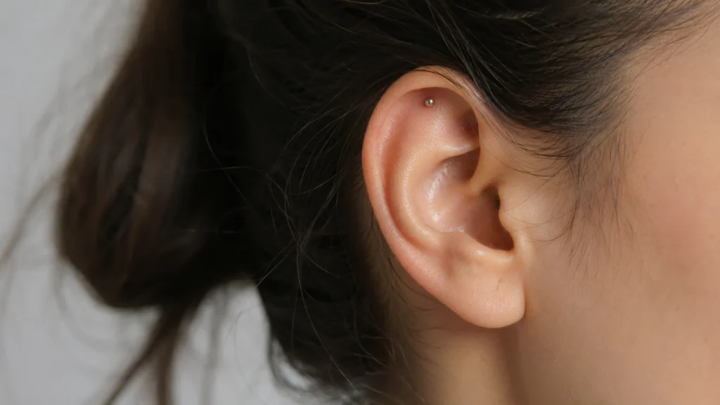 Close-up of an ear with a small hidden helix stud tucked into the upper cartilage fold