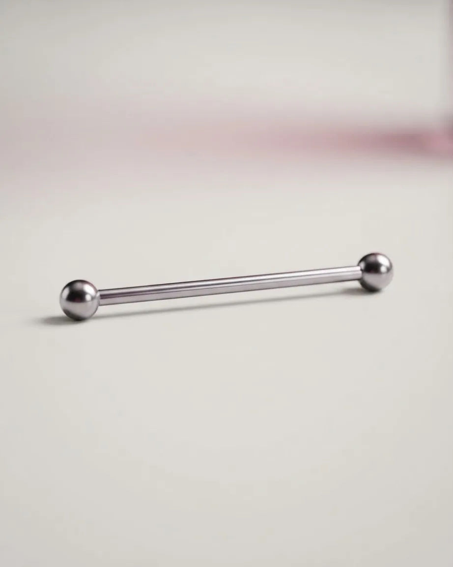 A polished silver industrial barbell with round ball ends rests horizontally on a smooth beige surface.